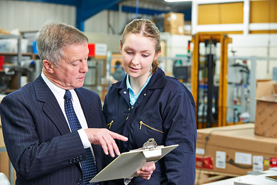 Ein Qualitätsingenieur erklärt Mitarbeiterin die Infos auf Klemmbrett